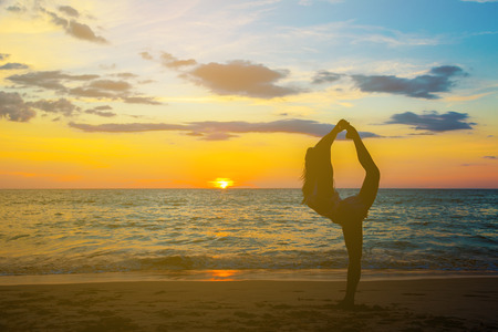 Silhouette woman with yoga posture on the sea beach at sunsetの写真素材