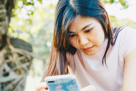 Young attractive girl using smartphone while sitting on a bench in the green park close up on handの写真素材