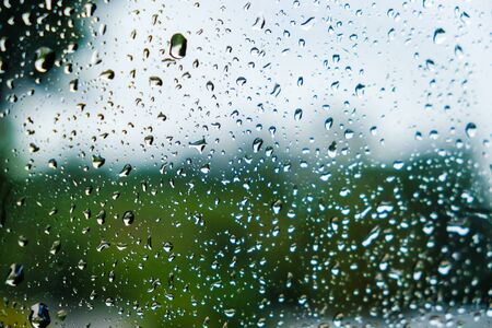 Drops of rain on window with blurred green nature background