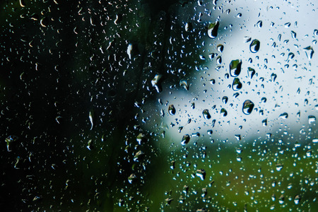 Drops of rain on window with blurred green nature background