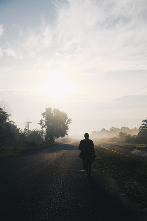 Buddha monk walking dhutanga for food donation in the morning sunrise on rural roadの写真素材