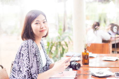 Asian young women use cellphone while sitting in coffee shop wood tableの写真素材