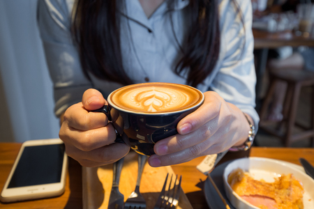 Business women hold cup of coffee latte in vintage cafeの写真素材