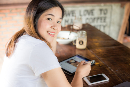 Happy young asian business women using tablet and cellphone while sitting in coffee shop on wood tableの写真素材