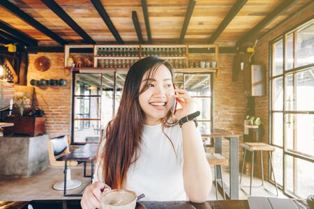 Smiling business women talking on smartphone holding coffee cup in vintage cafeの写真素材