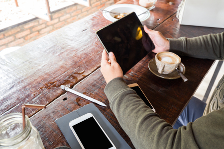 Man hand use tablet blank screen on wood table with hot latte, Rear view hand close upの写真素材