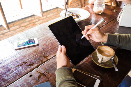 Man hand use tablet blank screen on wood table with hot latte, Rear view hand close up