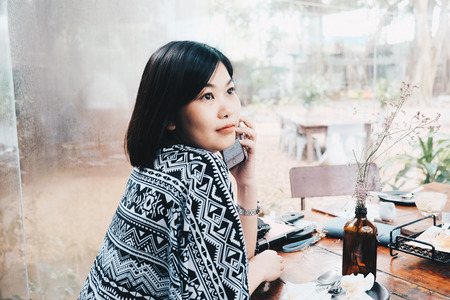 Business women use smartphone while sitting in cafe rear view smiling asian womenの写真素材