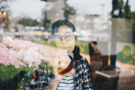 Glasses nerd asian women sitting in vintage coffee drinking ice teaの写真素材