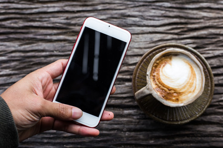 Smartphone with cup of coffee on wood background business objectの写真素材