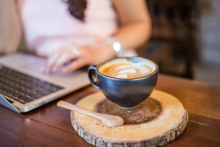 Hot latte art coffee with hand of business women use laptop on wooden table in cafeの写真素材