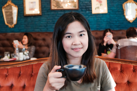Asian women hold black cup drinkking hot latte coffee in vintage cafeの写真素材