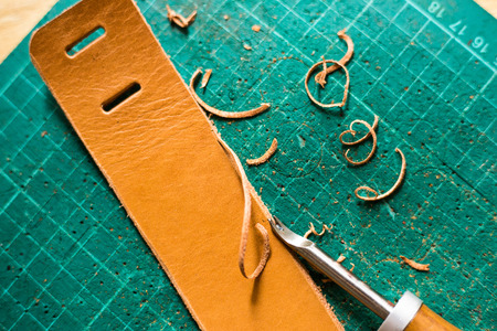 Leather work product with raw material on green board close up