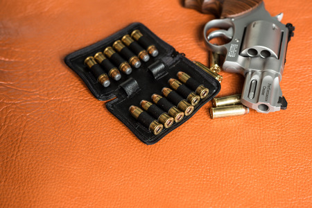 Revolver handgun with ammunition bullet on leather background