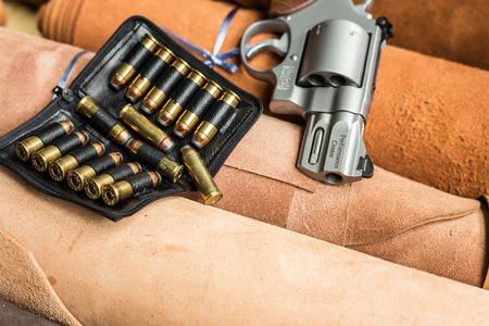Revolver handgun with ammunition bullet on leather background