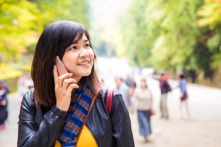 Young happy asian women talking on smartphone in the autumn park while travelの写真素材