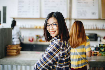 Smiling asian business women in coffee shop order latte coffee drinkの写真素材