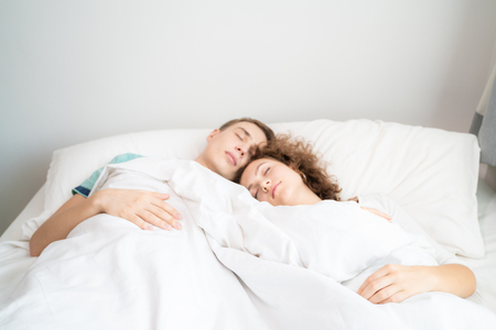 Beautiful young man and women love couple hugging on bed in morningの写真素材