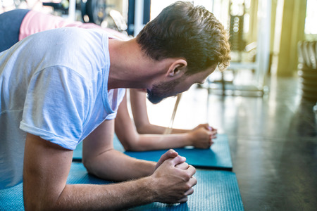 Portrait of sport active caucasian man doing plank position with women in gymの写真素材