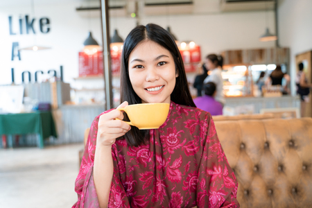 Young fashion women sittng on vintage sofa hold hot latte coffee in coffee shopの写真素材