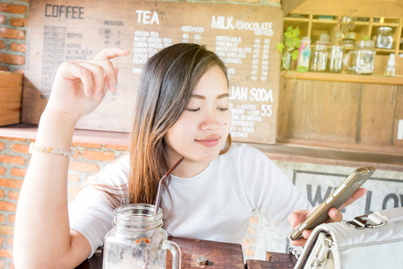 Beautiful asian business women use smartphone sitting in cafe drinking latte coffeeの写真素材