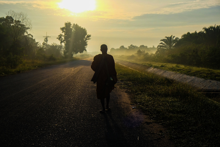 Buddhist monk walking on rural road morning sunriseの写真素材