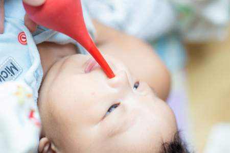 Father hand using bulb syringe nose clean infant baby boy on bedの写真素材