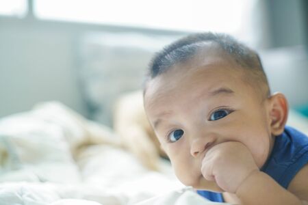 Adorable baby boy sucking finger lying on bed white blanketの写真素材