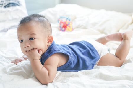 Adorable baby boy sucking finger lying on bed white blanketの写真素材
