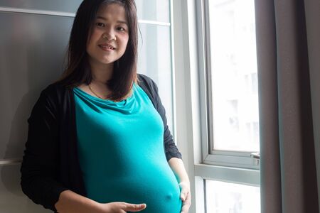 Pregnant women hold big belly stand in room near curtain, New baby conceptの写真素材