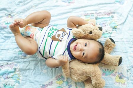 Toddler smiling asian child boy lying on bed enjy with doll