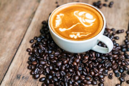 Latte art coffee in white cup with roast bean on wood tableの写真素材