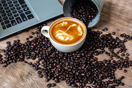 Latte art coffee cup and coffee bean with laptop computer on wood background top view