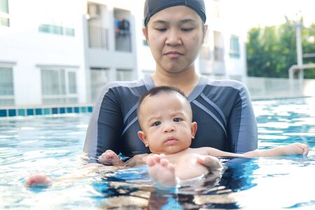 Mother training baby boy swimming in pool, Single momの写真素材