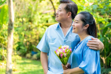 Happy senior couple relaxing in park holding flowerの写真素材
