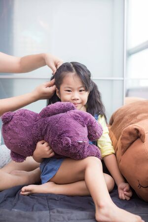 Mother doing hair style of her daughter with doll in cozy roomの写真素材