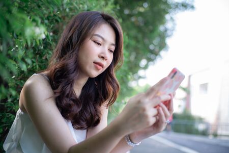Beautiful asian women use smart phone chat message in city park business technology