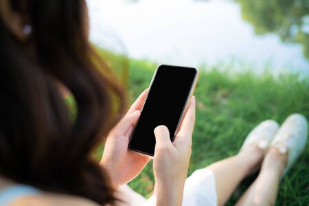 Beautiful women sitting on green grass use smartphone online chattingの写真素材