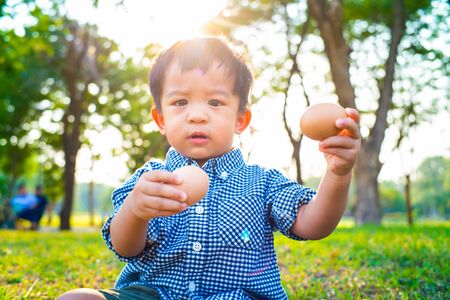 Adorable funny asian baby boy  playing on green grass with Easter eggs yellow boots shoeの写真素材