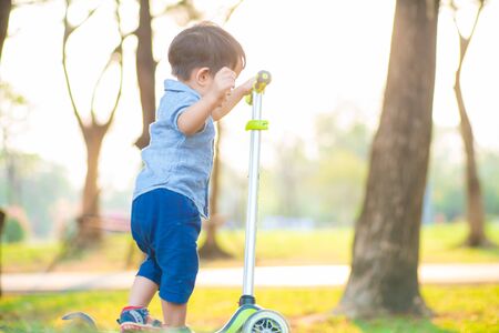 Little boy playing child scooter in city prak on green meadow sunset lightの写真素材