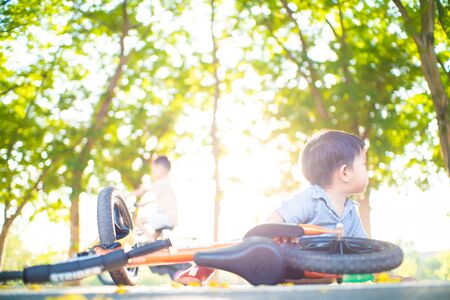 Asian boy falling balance bike accident on road in park tree forest outdoor activityの写真素材