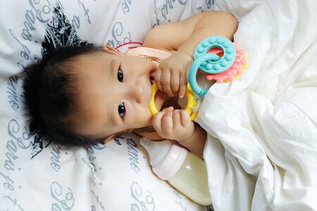 Asian baby boy lying on white blanket with rubber bite look down view