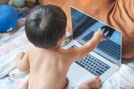 Happy baby boy playing laptop computer in bed room work from home conceptの写真素材