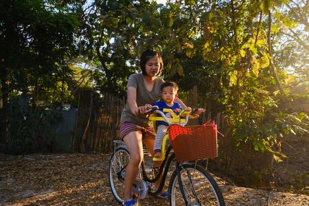 Baby boy ride bicycle with mother in rural road tree forest sunset light leisure outdoorの写真素材