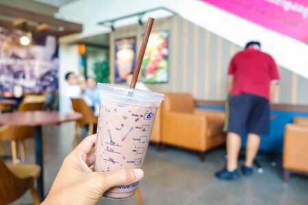 Ice coffee cup on wooden table in modern cafe blurred people background