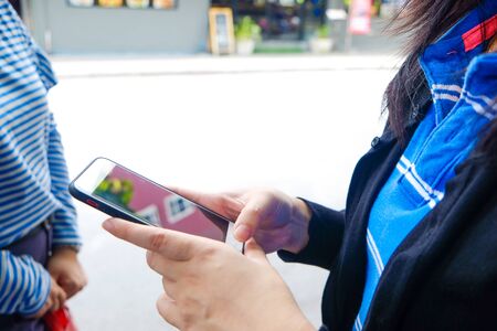 Women hand pointing finger on screen smartphone on street background in day atmospheric city,...