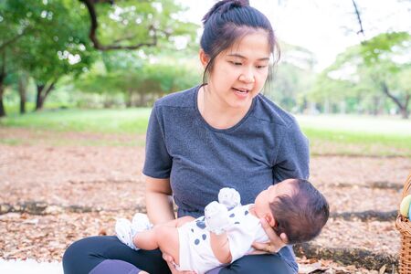 Mother with baby son leisure in city public park under tree