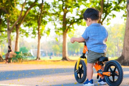 Adorable young boy riding bikes in the city park on asphalt road blurred green tree backgroundの写真素材