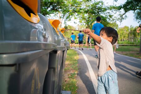 Little child boy throwing a plastic bottle into a recycle bin in city park, Save environmental conceptの写真素材