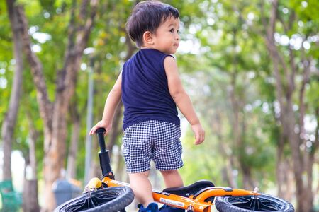 Adorable young boy riding bikes in the city park on asphalt road blurred green tree backgroundの写真素材